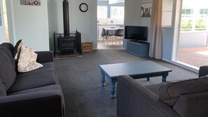 Ein Wohnzimmer mit einer Couch, einem Couchtisch, einem Fernseher, einem Kamin und Blick ins Freie.