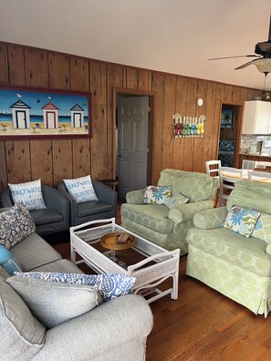 A living room with a wooden wall, a painting, a door, and a kitchen area.