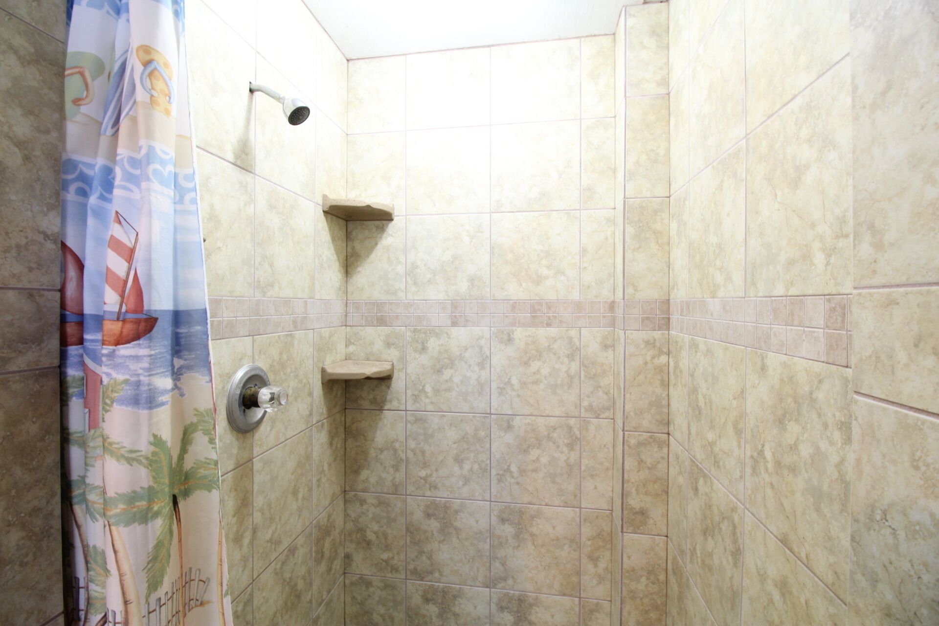 A shower area with beige tiles, a showerhead, and a small shelf.