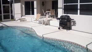 Ein Garten mit Swimmingpool, Gartenmöbeln und Grill.