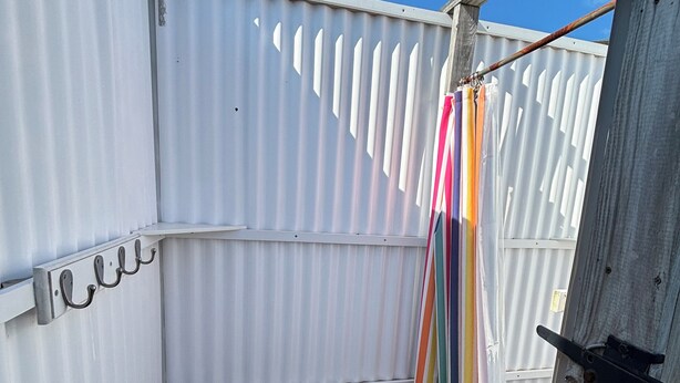 A small, enclosed outdoor space with a white metal fence, a white plastic chair, and a colorful striped curtain.