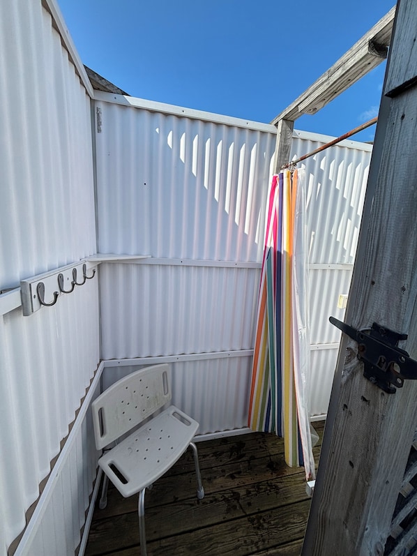 Un espacio exterior pequeño y cerrado, con una valla de metal blanco, una silla de plástico blanca y una cortina a rayas de colores.