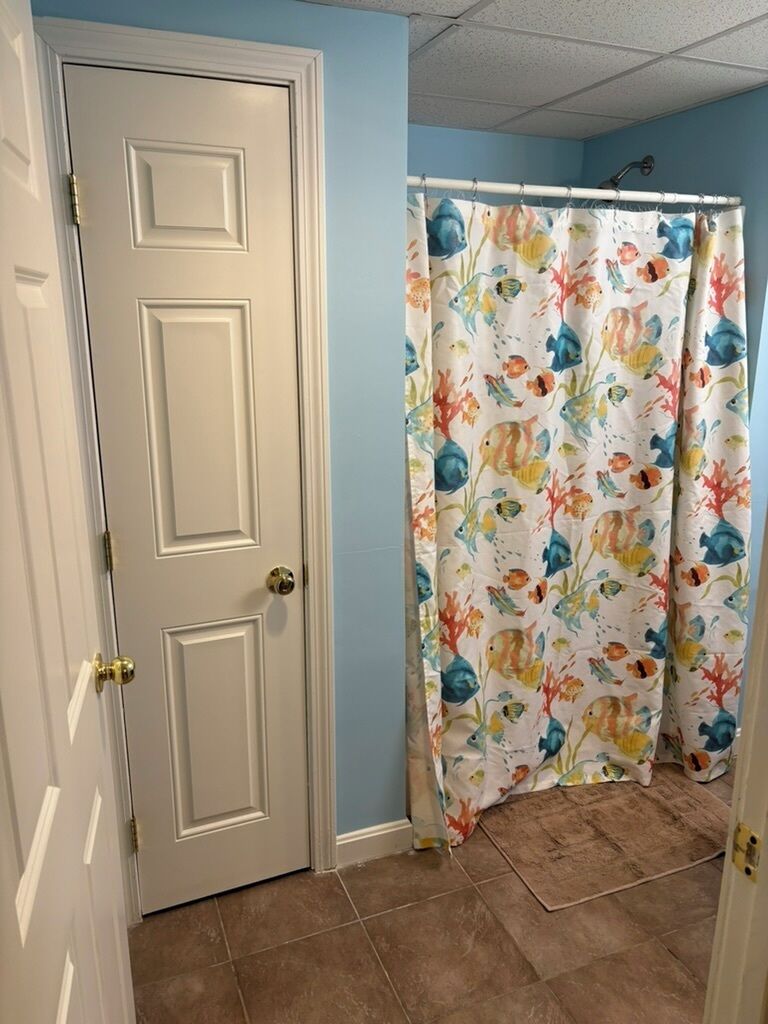 Een badkamer met een witte deur, een douchegordijn met een bloemenprint en bruine betegelde vloer.