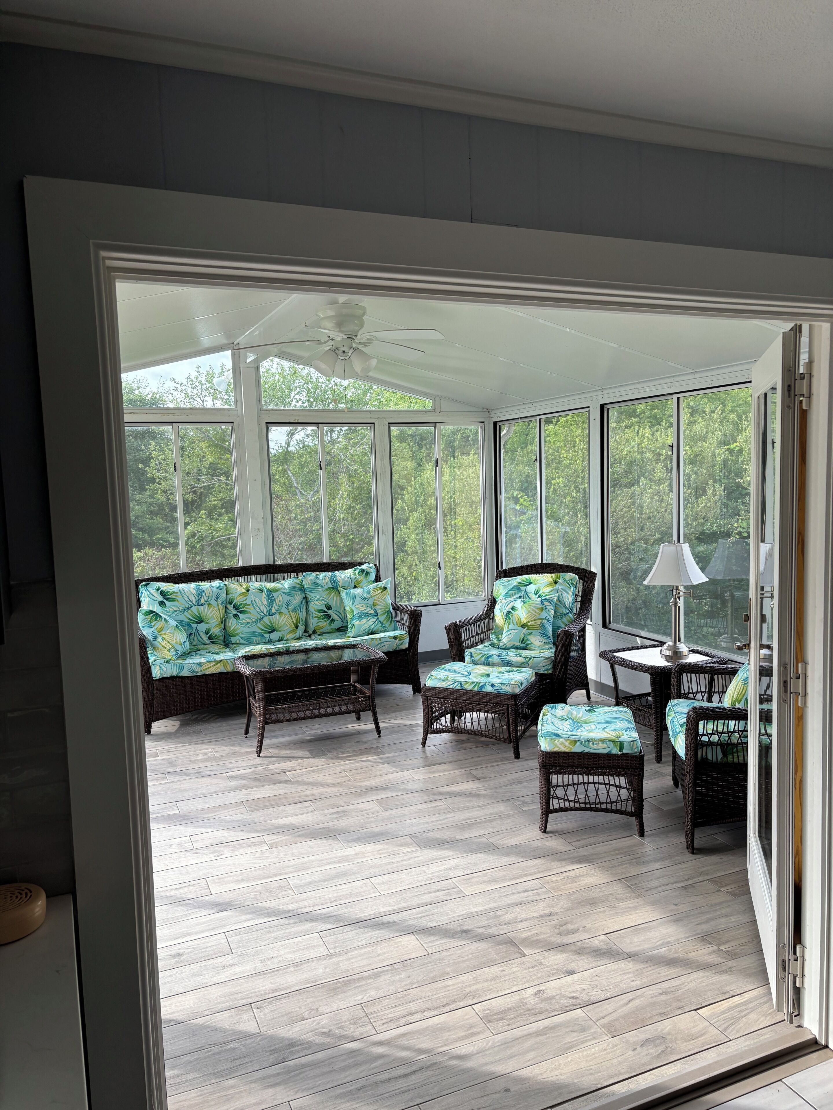 A sunroom with wicker furniture, large windows, and a ceiling fan.