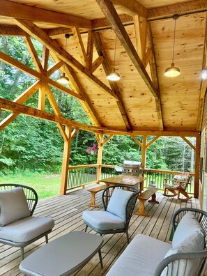 A wooden deck with outdoor seating, a grill, and a view of the surrounding forest.