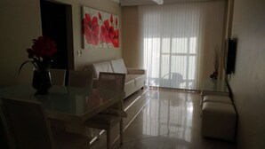 Ein modernes Wohnzimmer mit einem Glastisch, einer Couch und einem großen Fenster mit durchsichtigen Vorhängen.