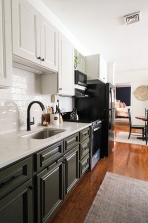 A modern kitchen with white cabinets, a black refrigerator, and a stainless steel sink.