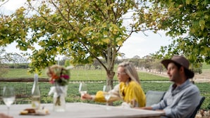 A dining table with a bottle, glasses, and a vase with flowers.