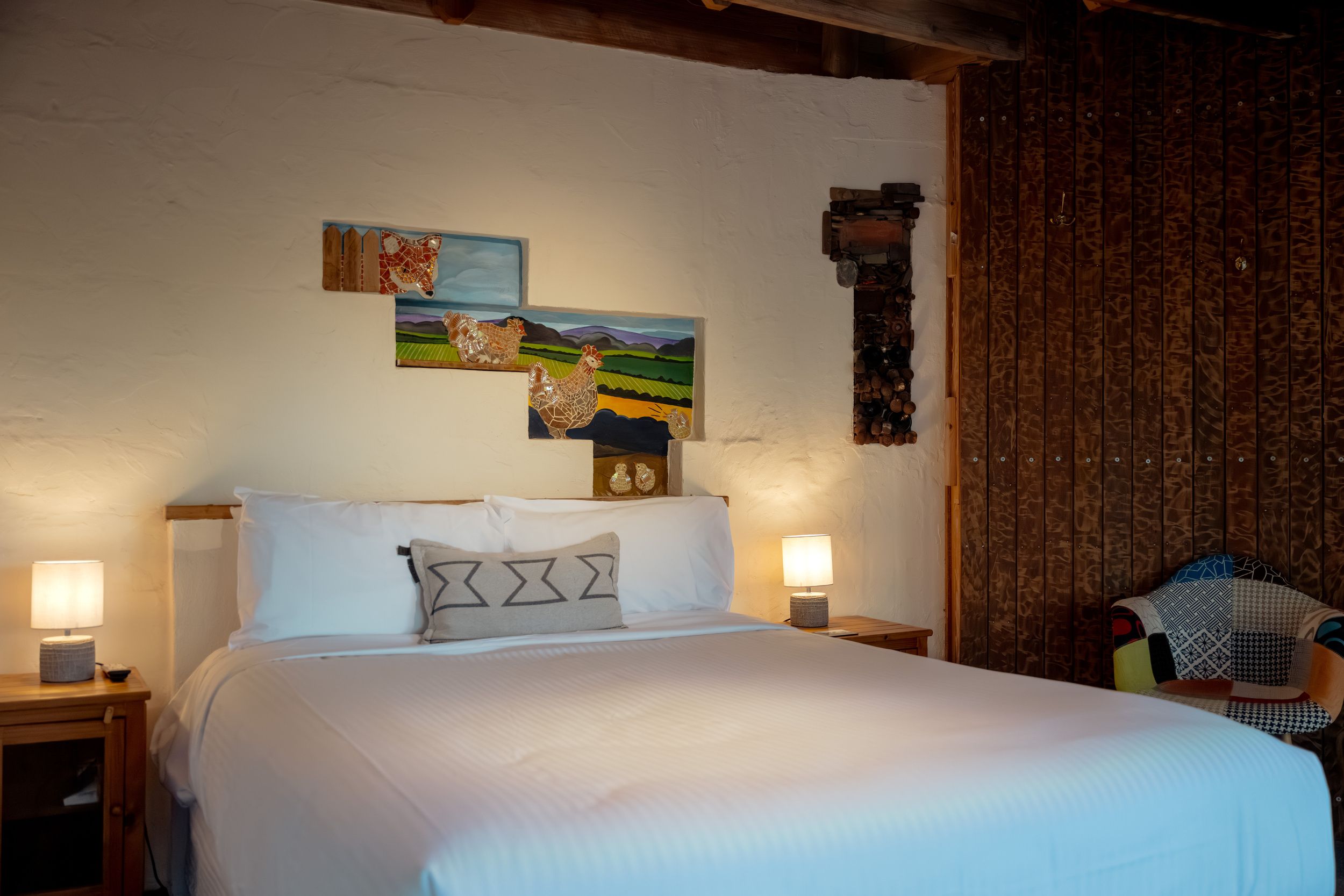 A neatly made bed with white linens and a patterned pillow, a wall-mounted clock, and two wall-mounted lamps on either side.