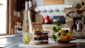 A kitchen counter with a bottle of wine, jars of preserves, and a bowl of fruit.