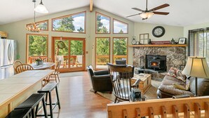 A spacious living area with a fireplace, wooden furniture, and large windows offering a view of the outdoors. - Escape to the Rockies!  3BR Cabin with Outdoor Space, Espresso Machine & Games!! (Bailey)