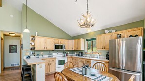 A modern kitchen with wooden cabinets, stainless steel appliances, and a central island with seating. - Escape to the Rockies!  3BR Cabin with Outdoor Space, Espresso Machine & Games!! (Bailey)