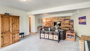A living room with a wooden cabinet, a coffee table with storage baskets, a television against a wooden wall, and a flag on the wall. - Escape to the Rockies!  3BR Cabin with Outdoor Space, Espresso Machine & Games!! (Bailey)