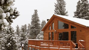 A wooden cabin with a deck and large windows, surrounded by snow-covered trees. - Escape to the Rockies!  3BR Cabin with Outdoor Space, Espresso Machine & Games!! (Bailey)