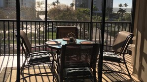 Un balcon avec une table et des chaises, donnant sur un paysage urbain avec de hauts immeubles et des palmiers.