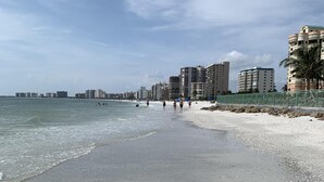 Une plage avec un rivage sablonneux, quelques personnes qui se promènent et des bâtiments en arrière-plan.
