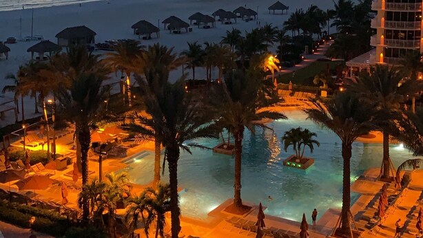 Un complexe hôtelier doté d’une piscine, de palmiers et offrant une vue sur la mer.