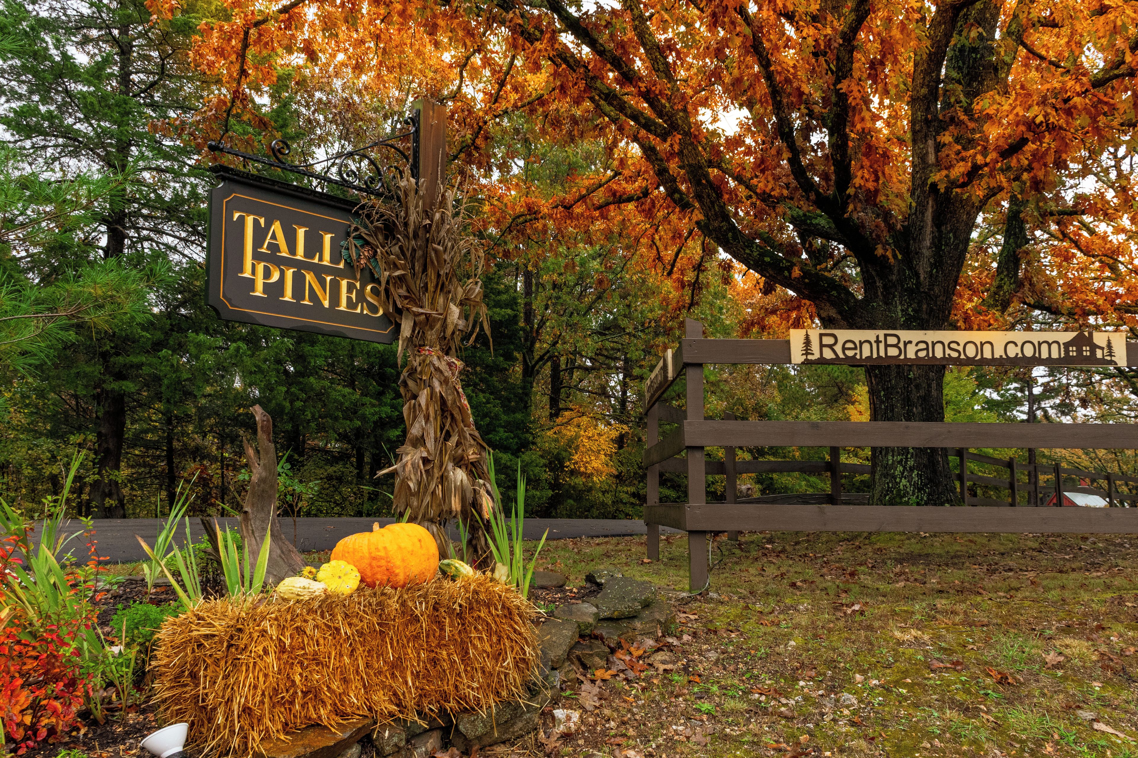 A sign for Tall Pines with a wooden fence and autumn foliage in the background.