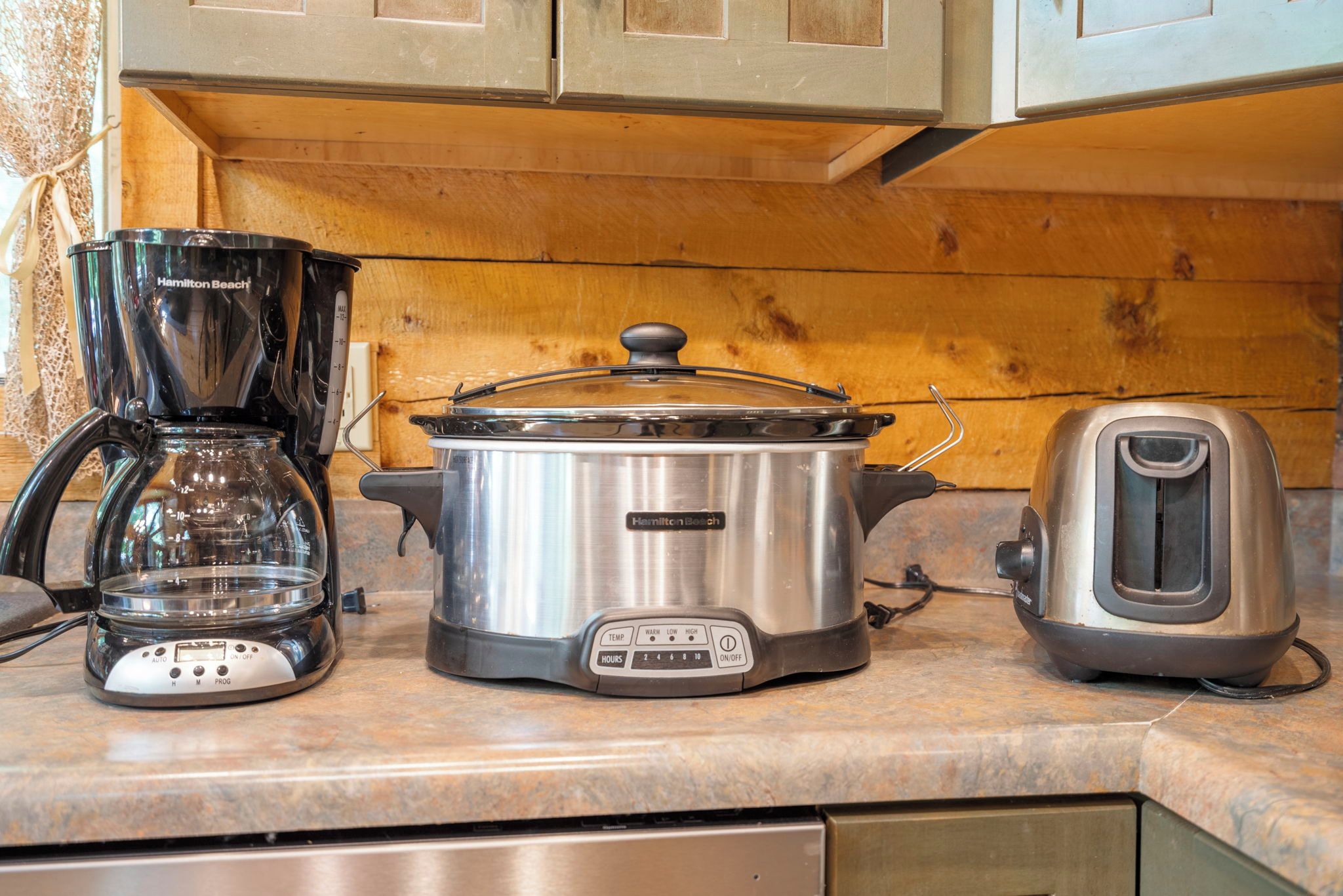 A kitchen with a Hamilton Beach coffee maker, a slow cooker, and a toaster on the counter.