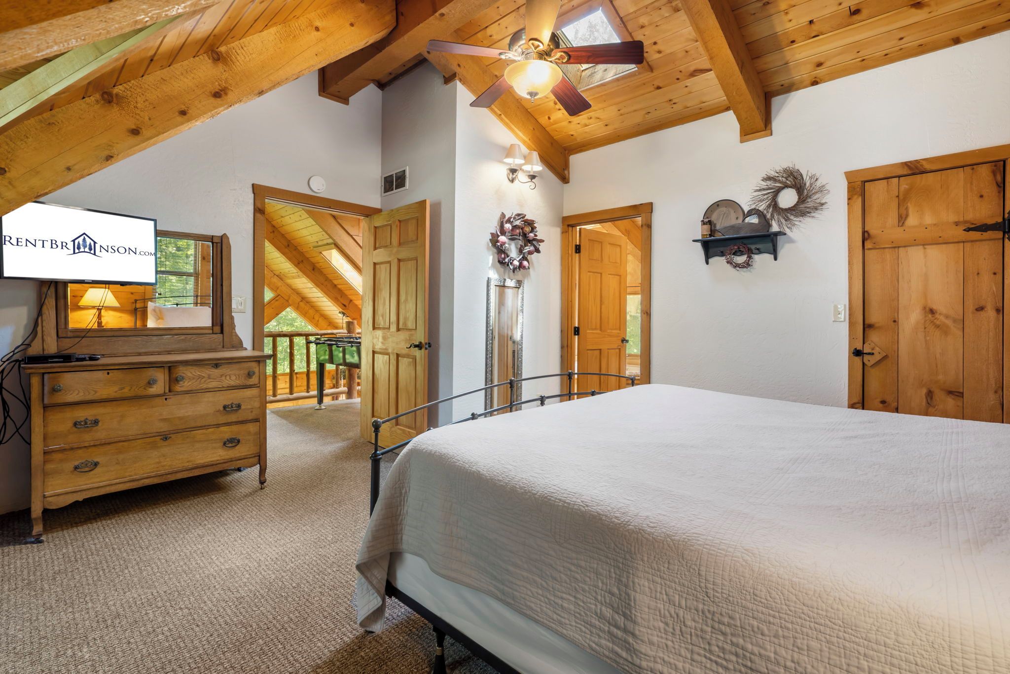 A bedroom with a bed, dresser, ceiling fan, and a view of the outdoors.