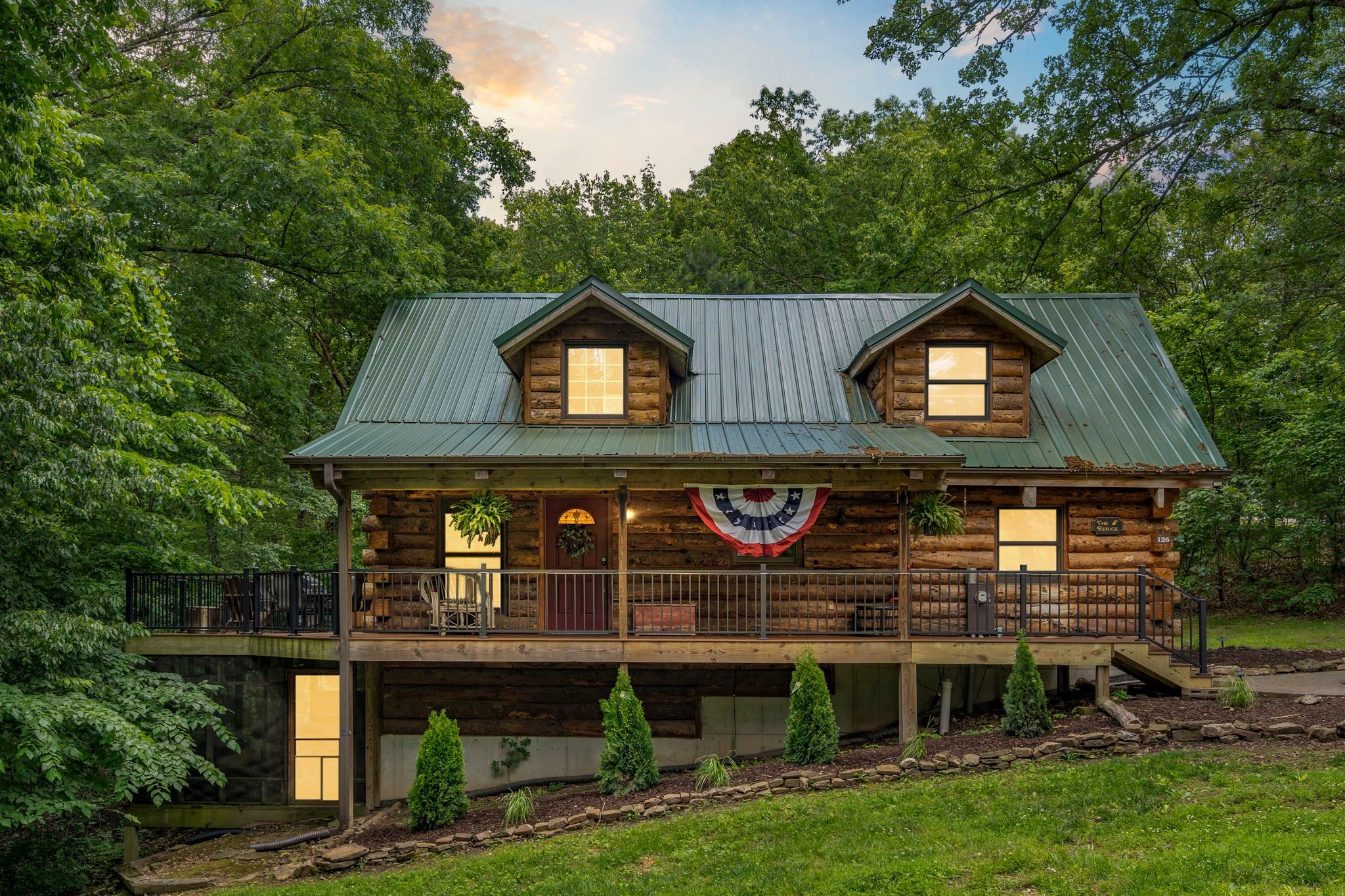 A log cabin with a porch, a flag, and a stone staircase leading to a deck.