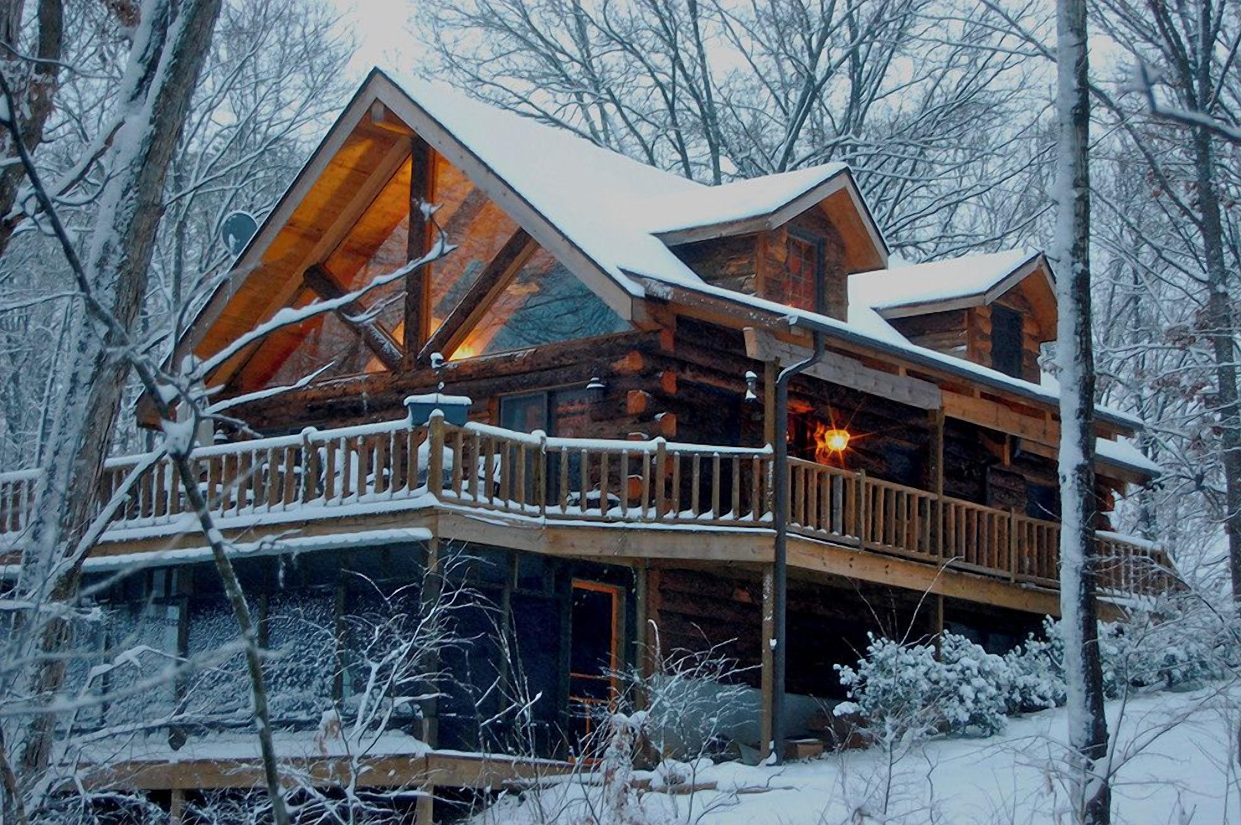 A log cabin with a balcony, surrounded by snow-covered trees.