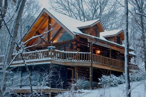 Una cabaña de troncos con balcón, rodeada de árboles cubiertos de nieve.
