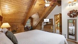 A cozy attic bedroom with a large bed, wooden ceiling beams, a ceiling fan, a mirror, and a view of the outside. - Private Engleman Spruce Cabin with Game Room, Community Pool & Car Charger (Blue Eye)