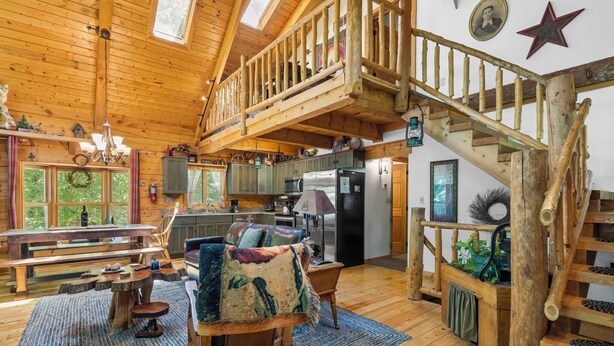 A rustic cabin interior with a wooden staircase, a dining area with benches, a kitchen with modern appliances, and a cozy seating area with a large chair and a blanket. - Private Engleman Spruce Cabin with Game Room, Community Pool & Car Charger (Blue Eye)