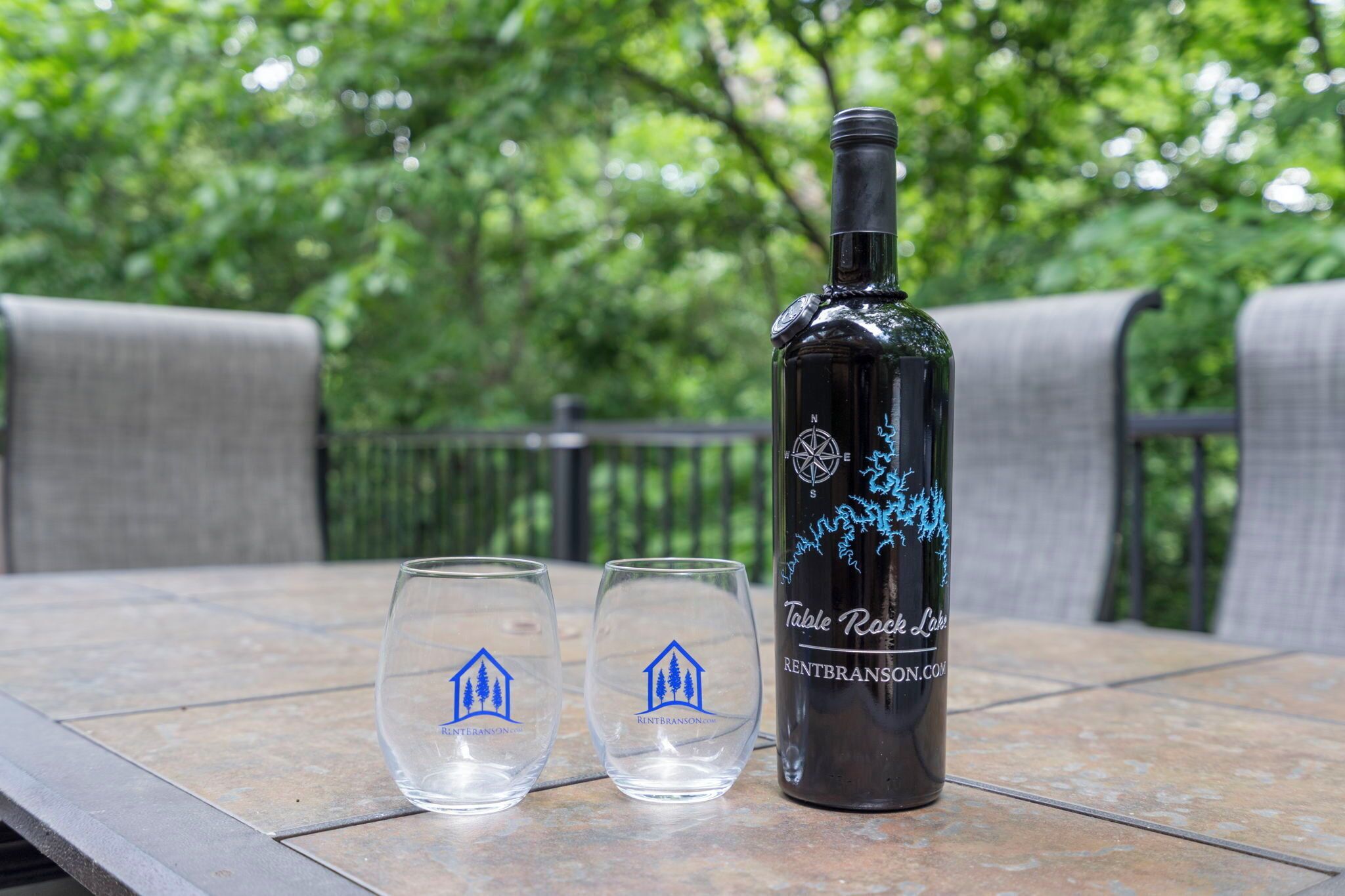 A bottle of wine and two glasses on a table with a view of trees in the background.