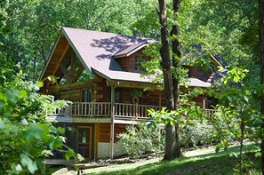 A log cabin with a balcony, surrounded by trees.