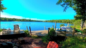 A lakeside dock with two chairs, a kayak, and a canoe.