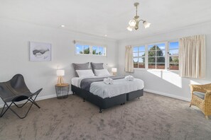 A bedroom with a bed, two bedside tables, a chair, a lamp, and a window with curtains. - Thermal Adventure - Plunge Pool, Sleeps 11 (Rotorua)