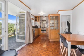 A kitchen with wooden cabinets, a dining table, and a view of the outdoors. - Thermal Adventure - Plunge Pool, Sleeps 11 (Rotorua)