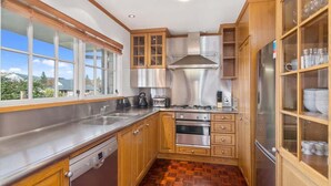A modern kitchen with wooden cabinets, stainless steel appliances, and a large window offering a view of the outdoors. - Thermal Adventure - Plunge Pool, Sleeps 11 (Rotorua)