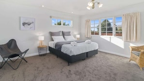 A bedroom with a bed, two bedside tables, a chair, a lamp, and a window with curtains. - Thermal Adventure - Plunge Pool, Sleeps 11 (Rotorua)