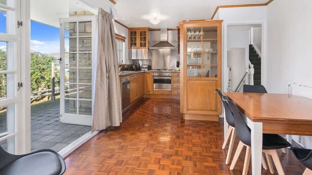 A kitchen with wooden cabinets, a dining table, and a view of the outdoors. - Thermal Adventure - Plunge Pool, Sleeps 11 (Rotorua)