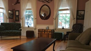 A living room with a wooden table, green sofa, and a brown armchair. There are two windows with curtains, a mirror on the wall, and a small wooden chest of drawers. - The coast of Maine a spacious 10 bedroom home. Equipped with an in ground pool (Saco)