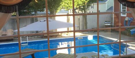 Un espace aménagé au bord de la piscine, avec vue sur celle-ci, comprenant une terrasse en bois et une table avec des verres et une carafe.