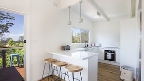 A modern kitchen with a large island, bar stools, a toaster, and a dishwasher. - Arthurs in Mollymook (Mollymook Beach)
