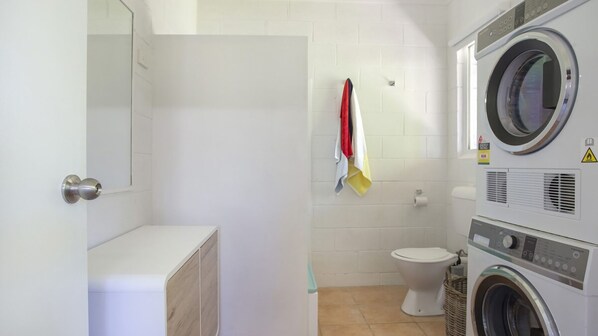 A compact laundry room with a washing machine, a dryer, and a toilet. - Arthurs in Mollymook (Mollymook Beach)
