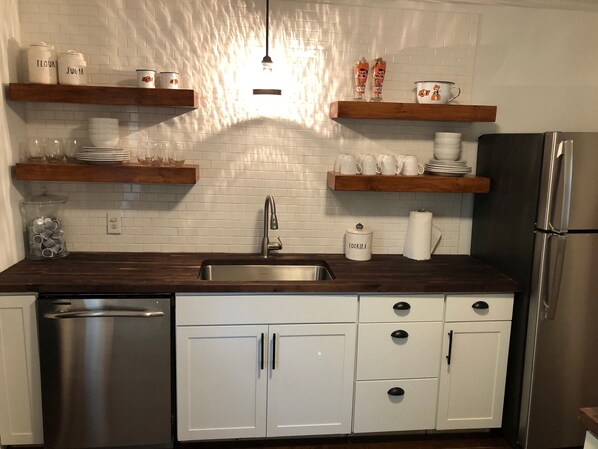 A modern kitchen with white cabinets, stainless steel appliances, wooden shelves, and a tiled backsplash.