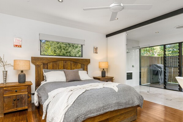 A modern bedroom with a wooden bed, two bedside tables, a ceiling fan, and a large window.