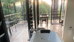 Ein modernes Badezimmer mit einer großzügigen Badewanne, einer Duschkabine aus Glas sowie Blick auf die Terrasse und den Garten.