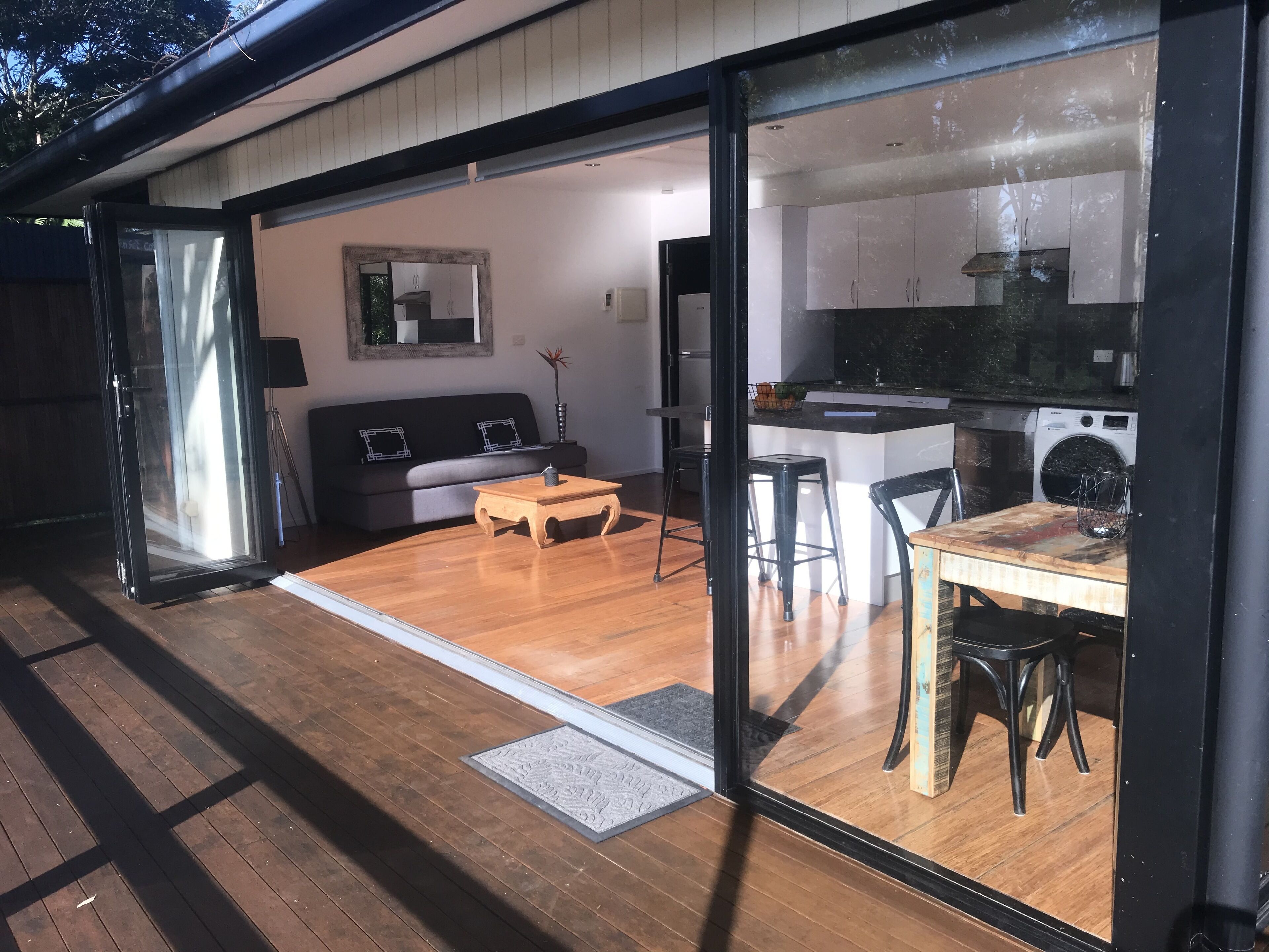 Un espacio habitable moderno de concepto abierto con suelo de madera, un sofá, una mesa de centro y una zona de cocina con lavadora.