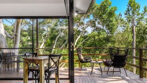 Eine Holzterrasse mit Gartenmöbeln, einer Glaswand und Blick auf Bäume.