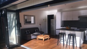 Ein modernes Interieur mit Holzboden, einer Couch, einem Couchtisch und einer Küchenzeile mit Kühlschrank und Barhocker.