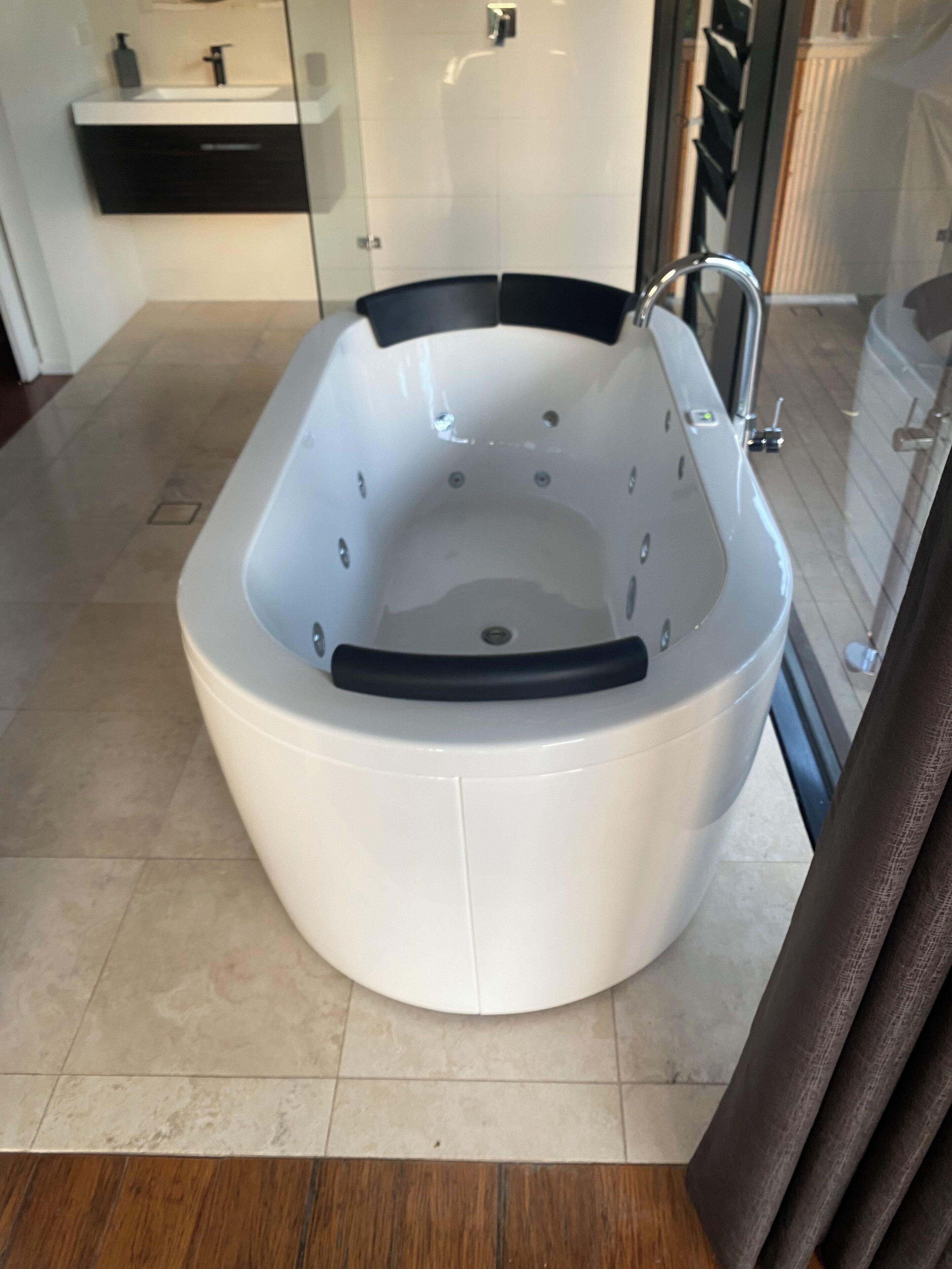 Een moderne badkamer met een vrijstaand bad, een douchecabine van glas en een zwart wastafelmeubel met een wastafel en zeepdispenser.