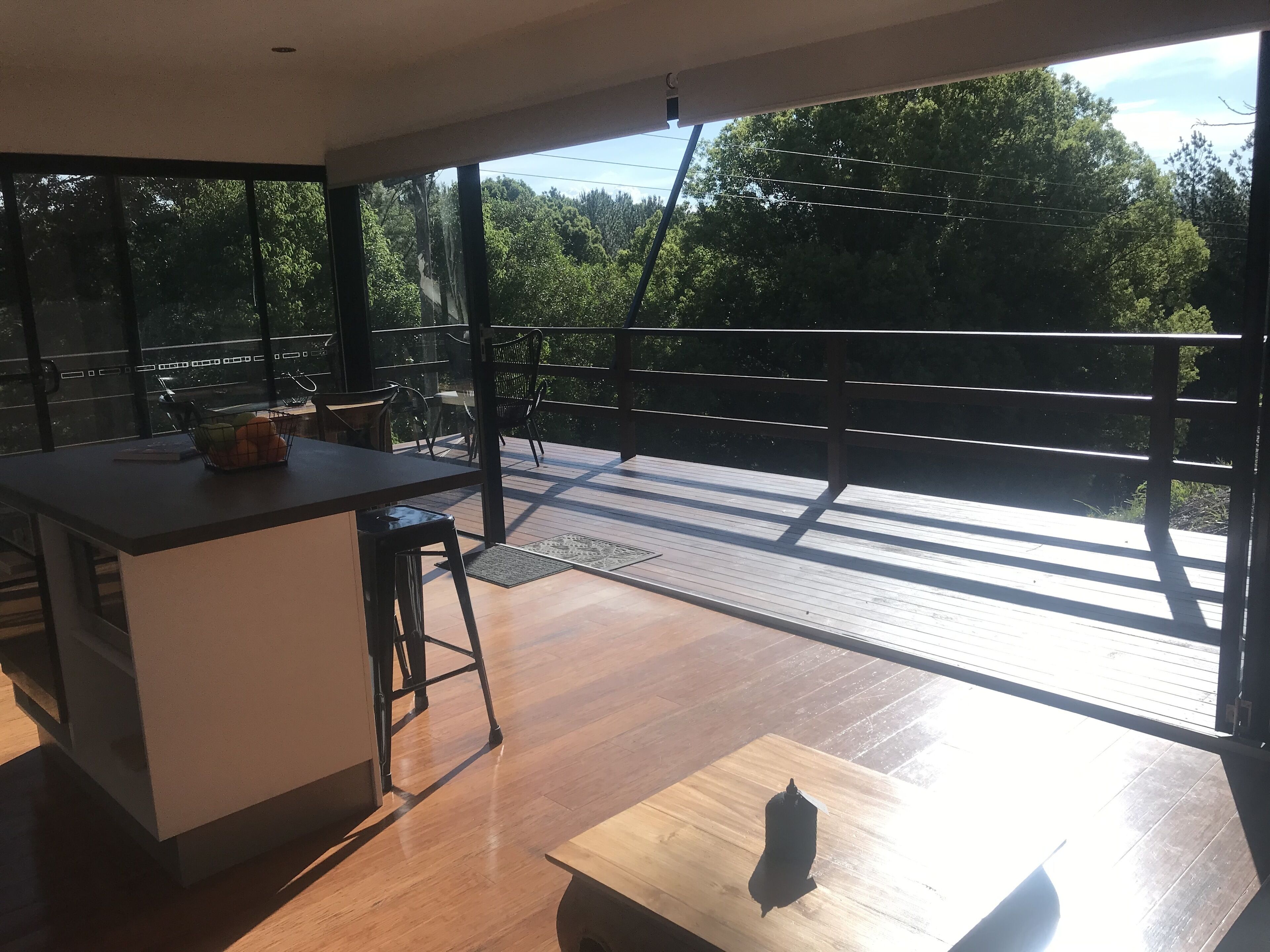 A modern kitchen with a large island, a dining area with a table and chairs, and a balcony with a wooden deck and railing.