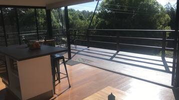 A modern kitchen with a large island, a dining area with a table and chairs, and a balcony with a wooden deck and railing.
